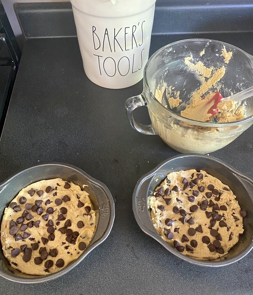 Two round cake pans with cookie dough for cookie cakes before baking.