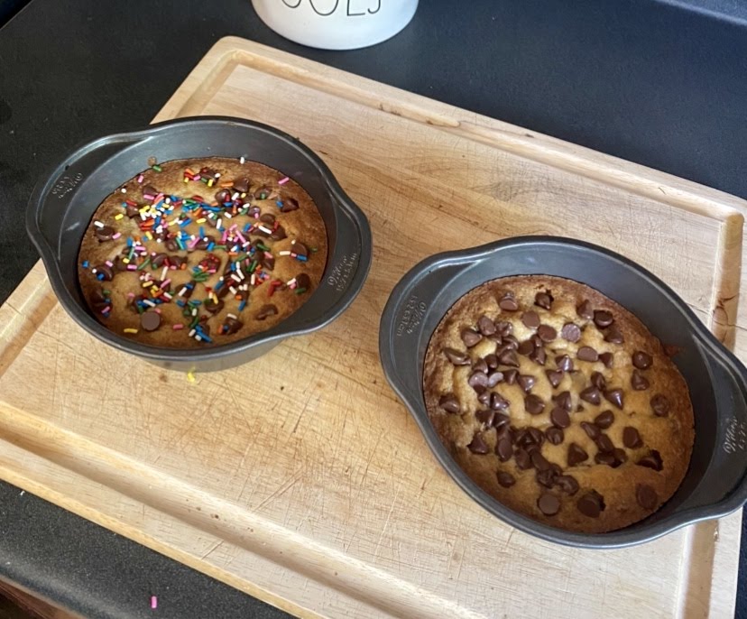 Two round cake pans with cookie dough for cookie cakes after baking.