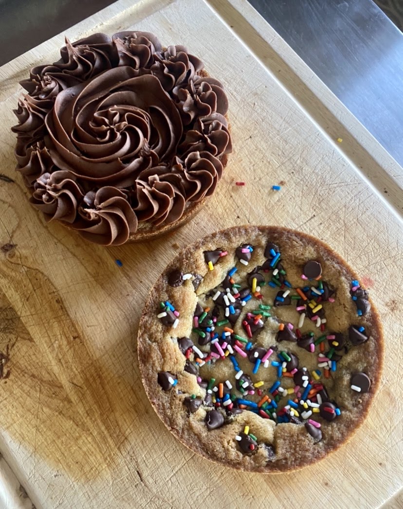 Two round cookie cake layers, one with sprinkles, and the other with piped chocolate frosting. 