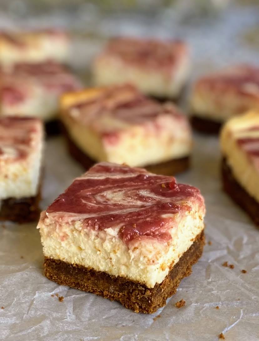 gingerbread cheesecake bars with cranberry swirl cut into squares on  parchment paper