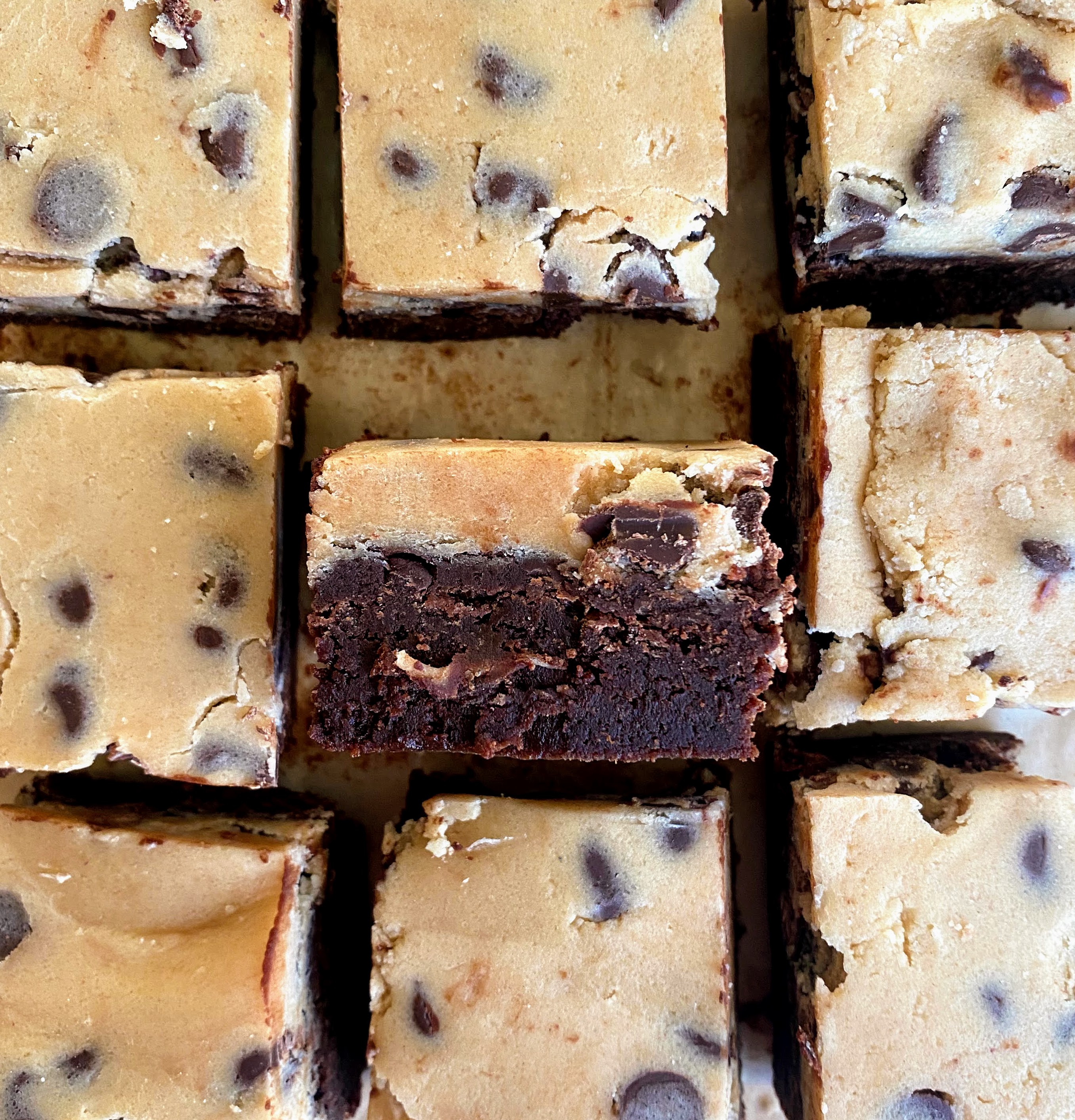 cut chocolate chip cookie dough brownie bars on a baking sheet with on turned on its side so you can see the layers