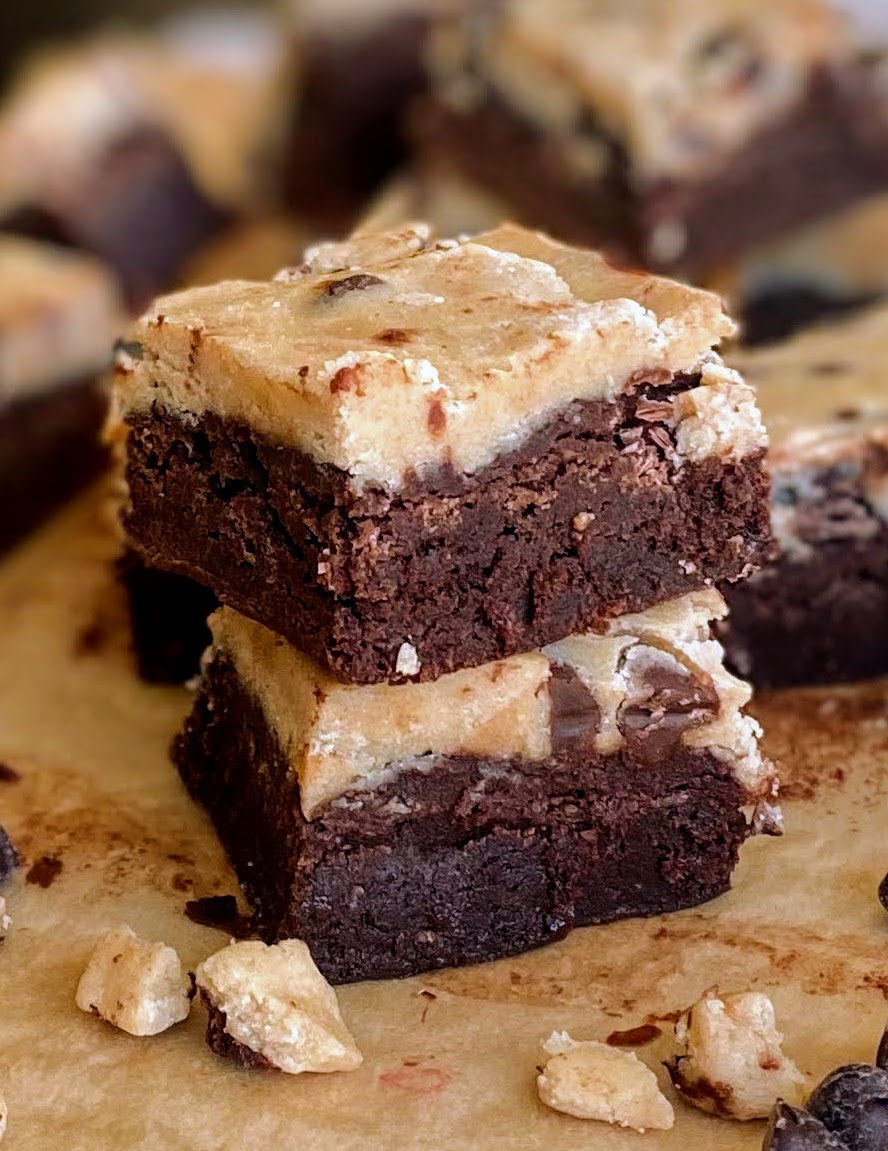 chocolate chip cookie dough brownies sliced and stacked on top of each other on parchment paper