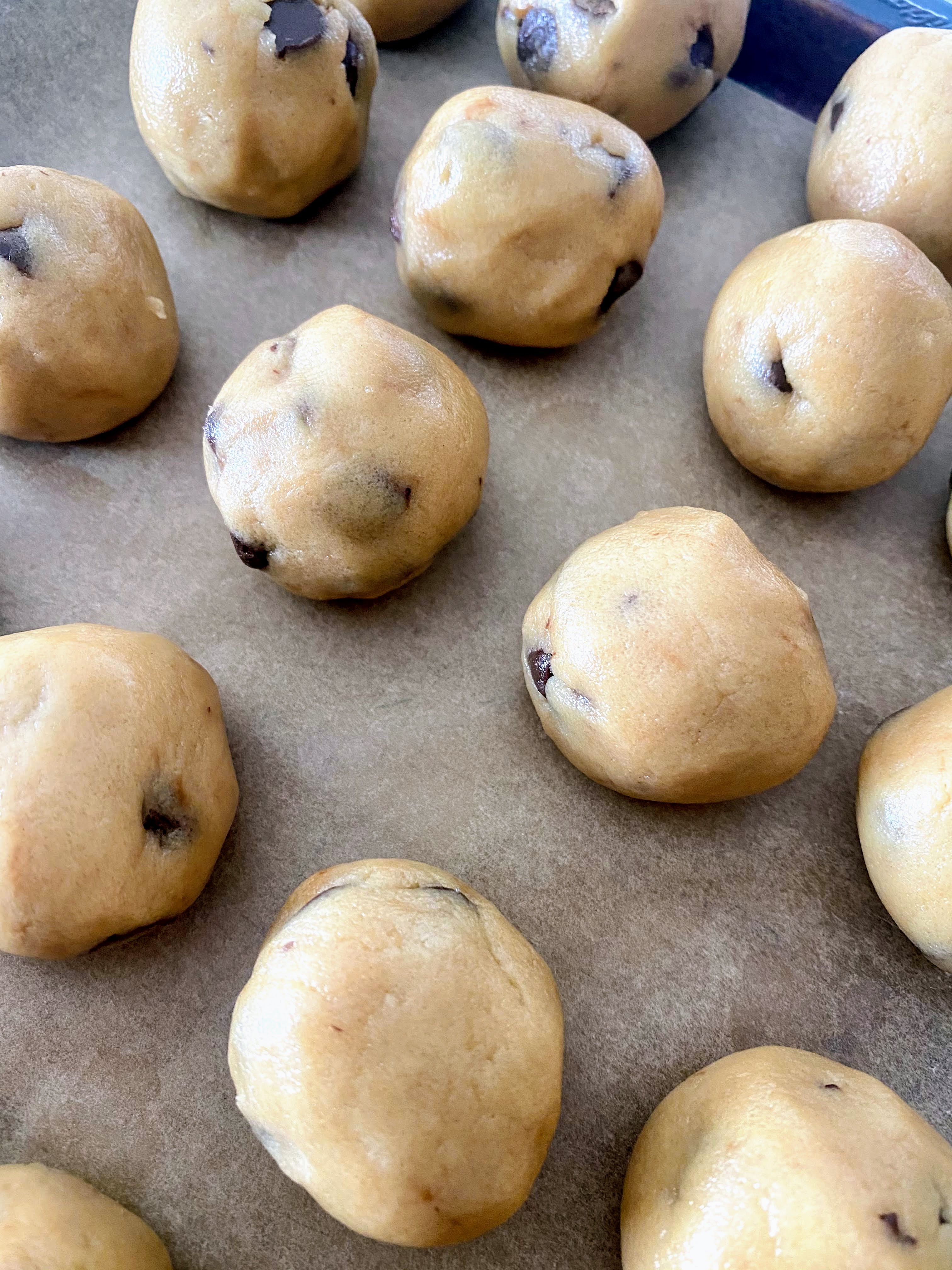 Edible cookie dough rolled into balls on a baking sheet. 