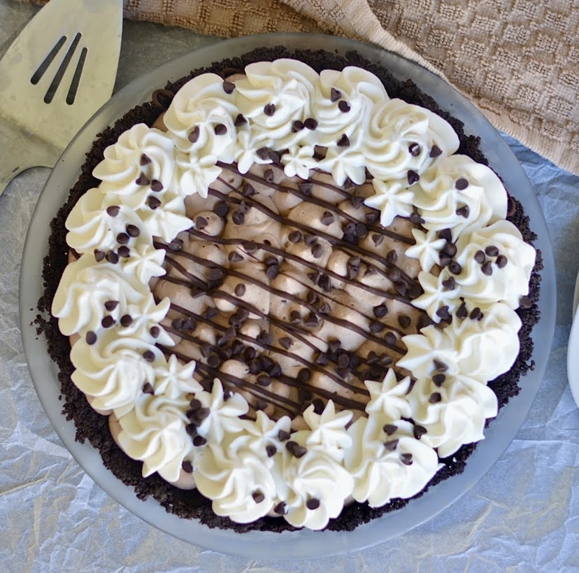 a whole chocolate cream pie topped with whipped cream, chocolate drizzle, and chocolate chips