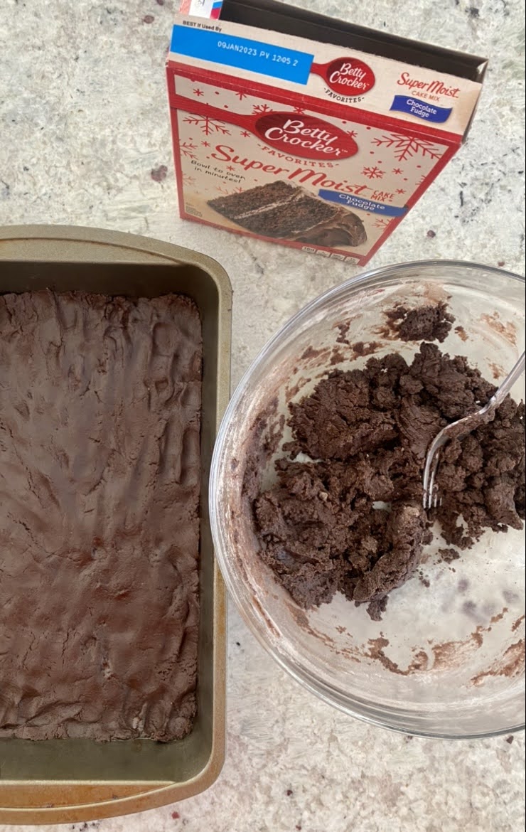 a baking pan with chocolate dough pressed into it, a box of cake mix, and the remaining dough in a glass bowl