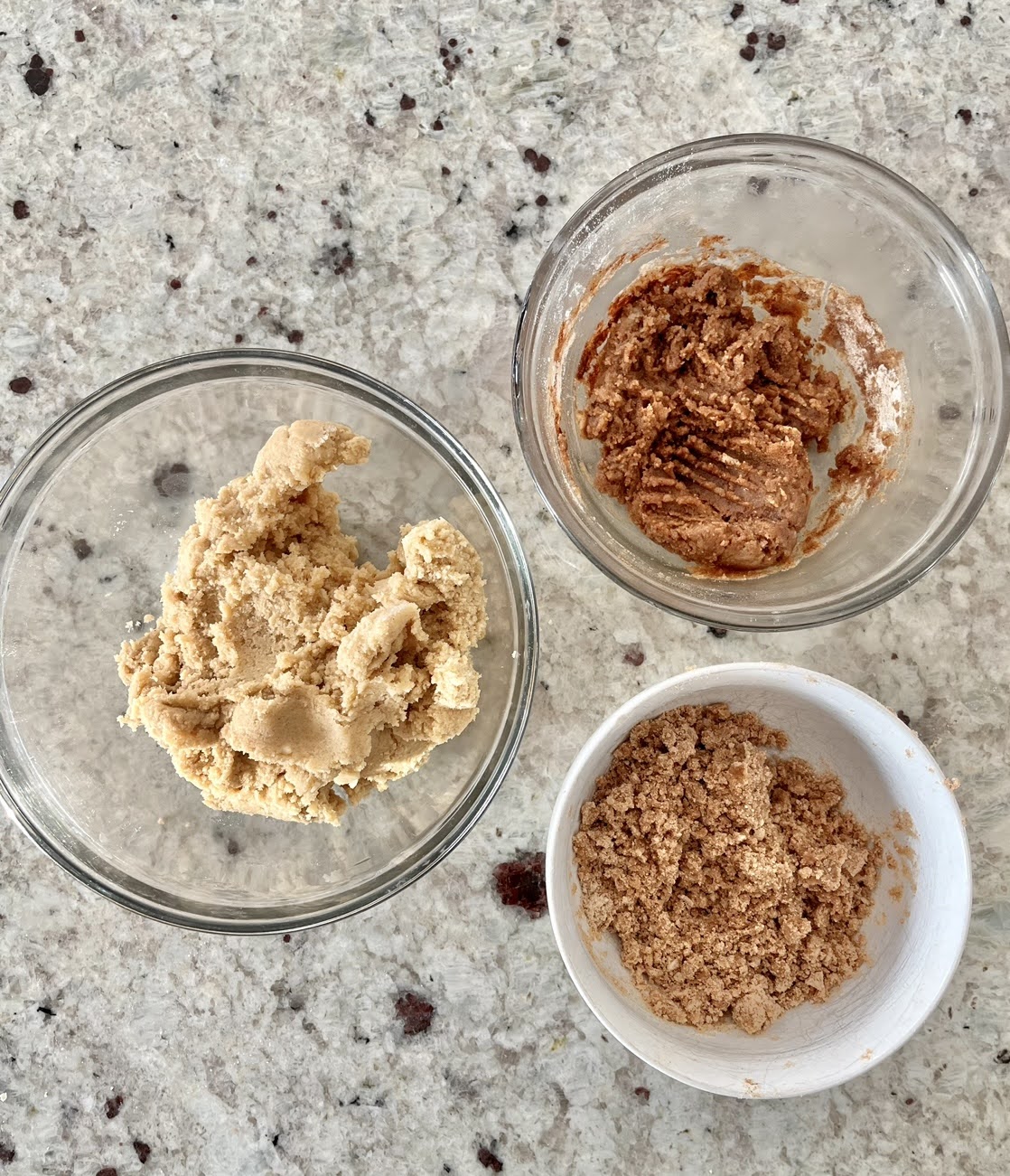 A countertop with three containers showing each: cookie dough, cinnamon filling, and streusel topping. 