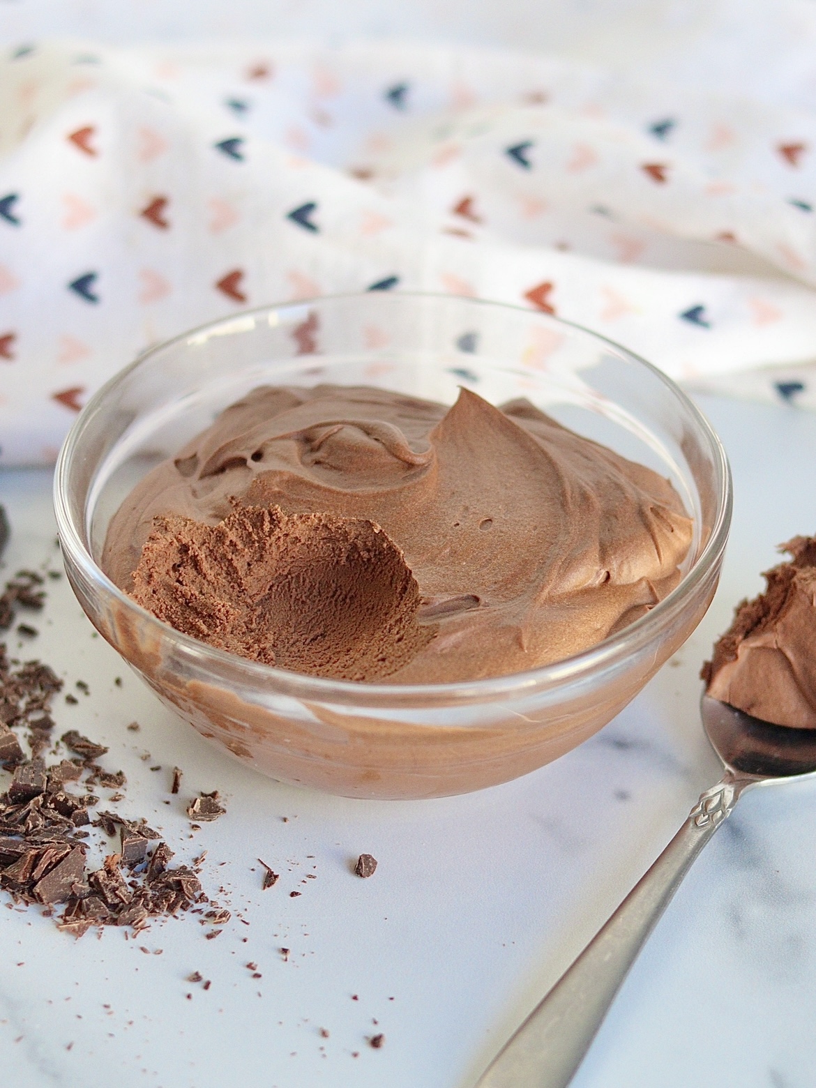 A bowl of two ingredient chocolate mousse with a spoonful taken out of it surrounded by chocolate shavings