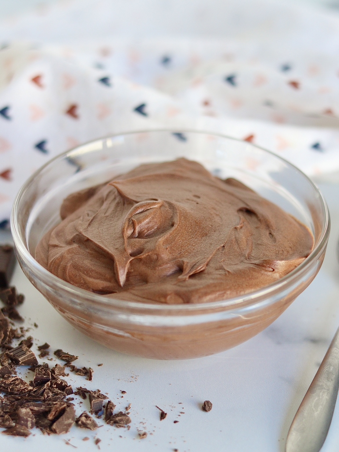 A bowl of two ingredient chocolate mousse with chocolate shavings and a spoon next to it