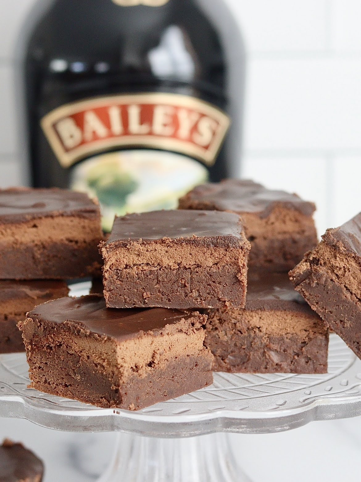 a stack of irish cream brownies on a cake plate with a bottle of Bailey's in the background