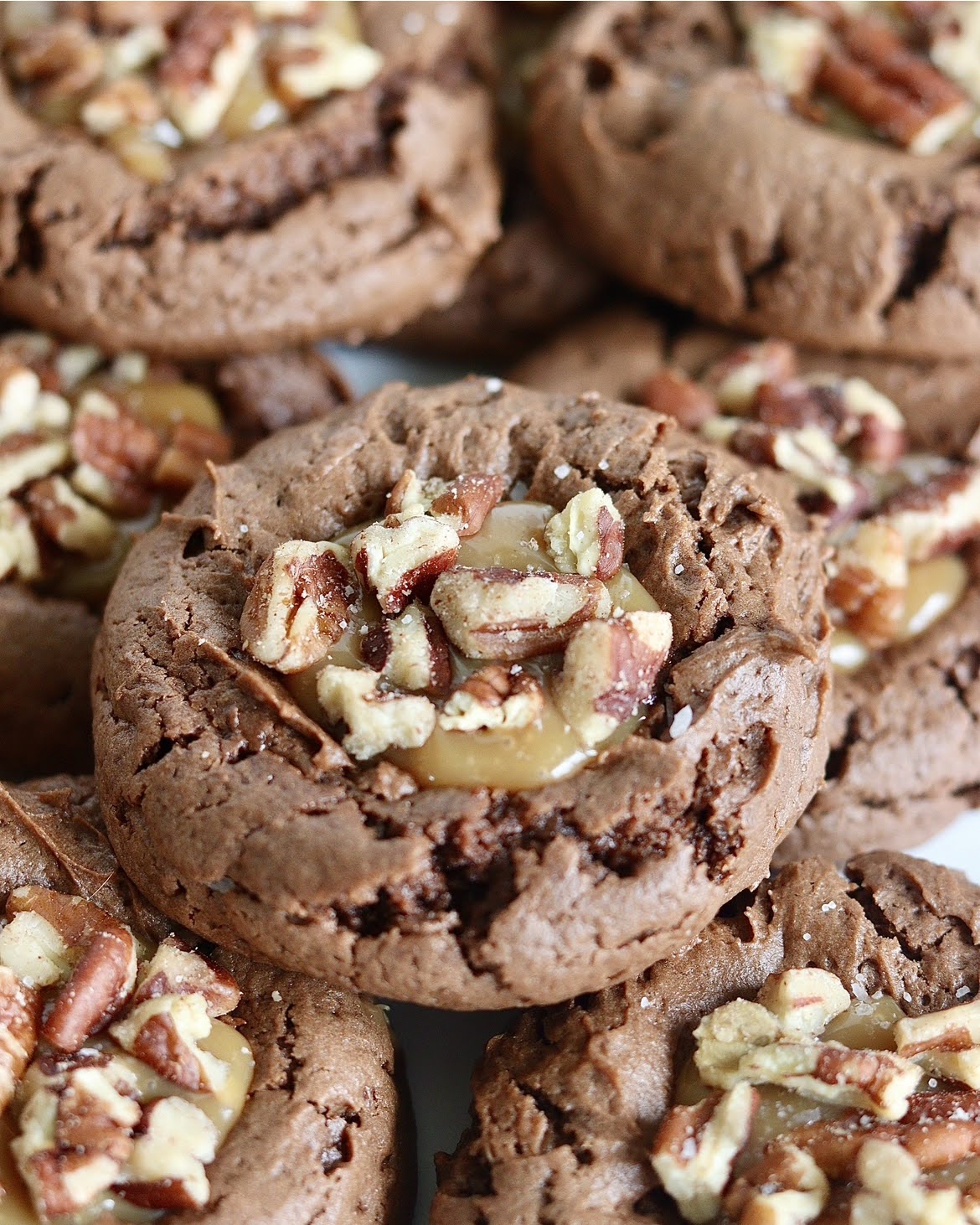 a close up shot of a chocolate cookie filled with caramel and pecans