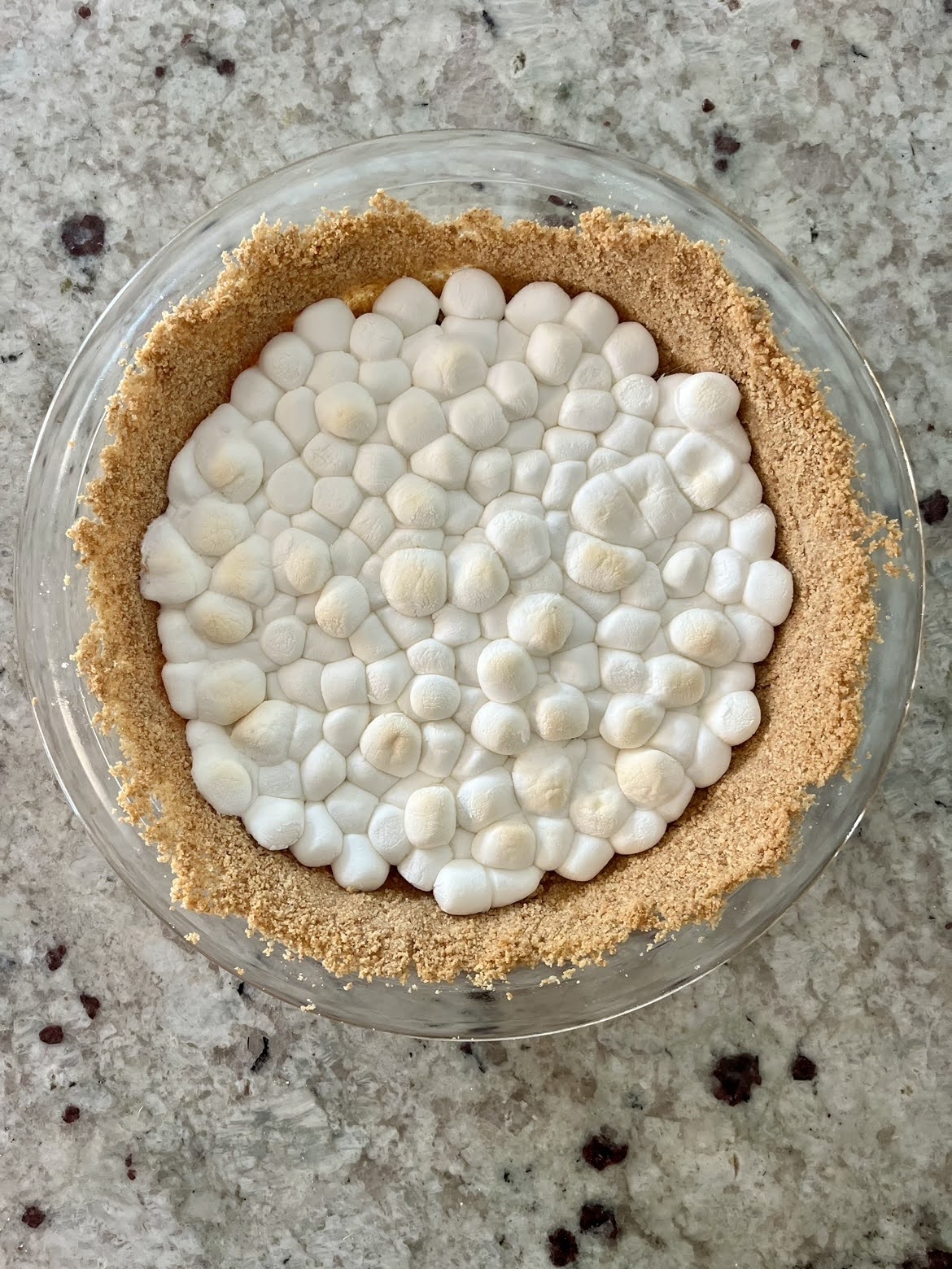 A process photo of a prepared graham cracker crust with a melted marshmallow layer.