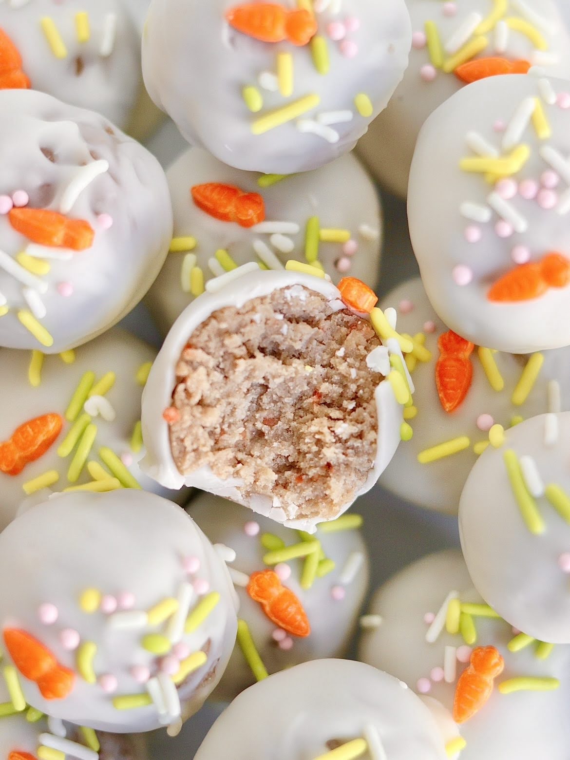 A final photo of a carrot cake truffle with a bite taken out of it, coated in white chocolate and sprinkles.