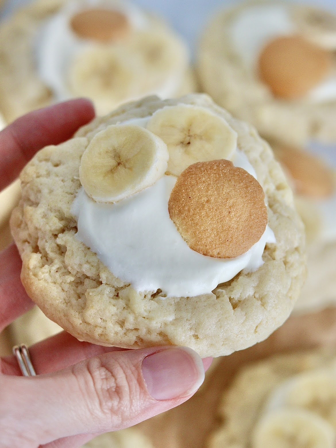 An up-close photo of a hand holding a banana cream pie cookie topped with sliced bananas and a small Nilla Wafer Cookie.
