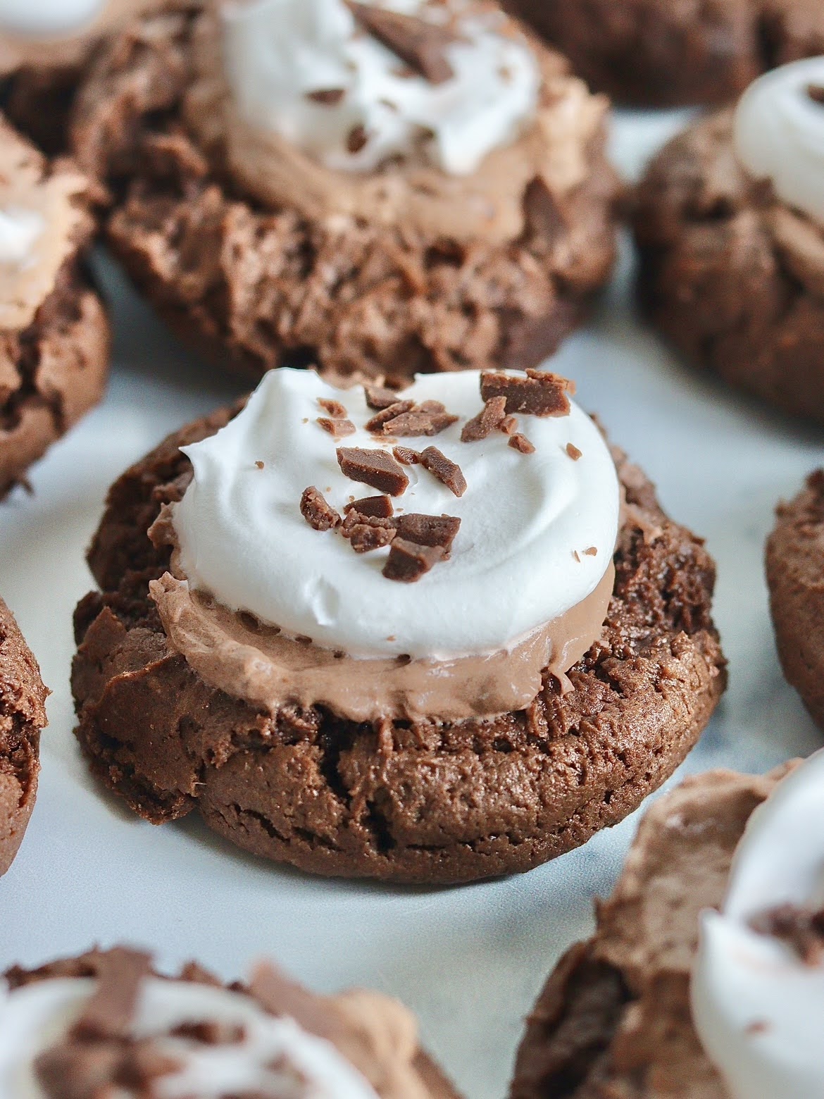 A close up photo of a French Silk Pie cookie. A soft chocolate cookie topped with chocolate cream, whipped cream and chocolate pieces.