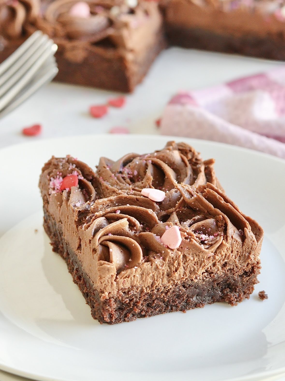 plated slice of frosted brownie, frosted with chocolate frosting swirls and heart-shaped sprinkles